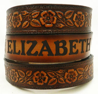 Children's custom leather name belt featuring embossed floral design with engraved nameplate, handcrafted in warm brown leather.