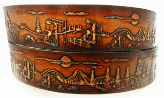 A brown leather belt with an oilfield design, featuring engraved scenes of oil rigs and a sunset.